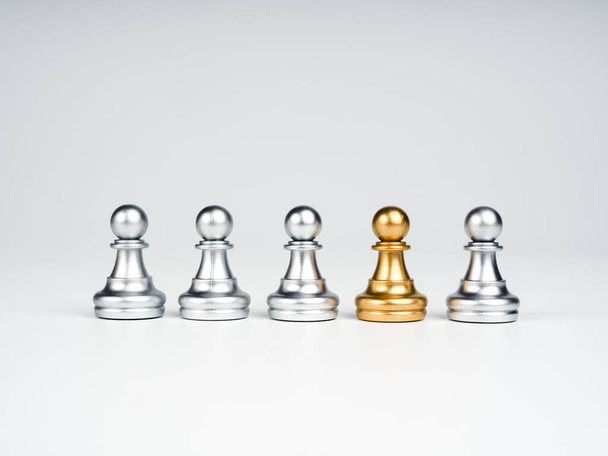 Z davu vyčnívá figurka zlatého pěšáka, který vyčnívá ze skupiny stříbrných šachových figurín na bílém pozadí. Leadership, Unique, influencer, difference concept. - Fotografie, Obrázek