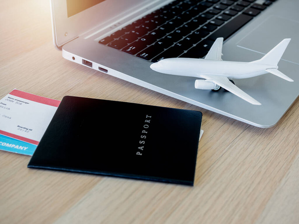 biały samolot zabawka na laptopie komputer z paszportem czarny okładka i bilet lotniczy na drewnianym biurku. Rezerwacja biletów online dla koncepcji podróży. - Zdjęcie, obraz