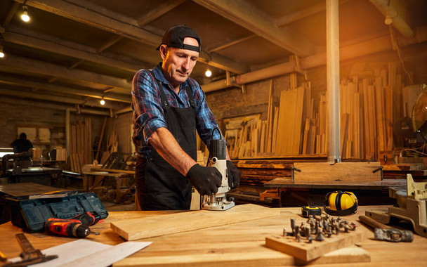 Vezető profi asztalos a kézi marógép egyenletes munkájában az ácsműhelyben - Fotó, kép