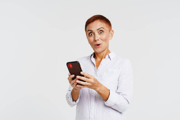Shocked senior woman with short hair using mobile phone isolated over white background - Photo, Image