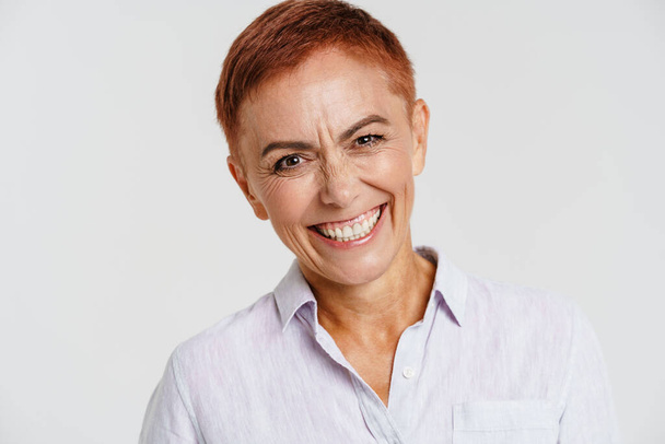 Ginger senior woman with short hair smiling and looking at camera isolated over white background - Zdjęcie, obraz