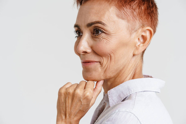 Ginger senior woman with short hair smiling and looking aside isolated over white background - Foto, afbeelding