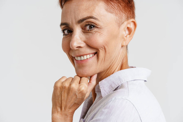 Ginger senior woman with short hair smiling and looking at camera isolated over white background - Фото, изображение