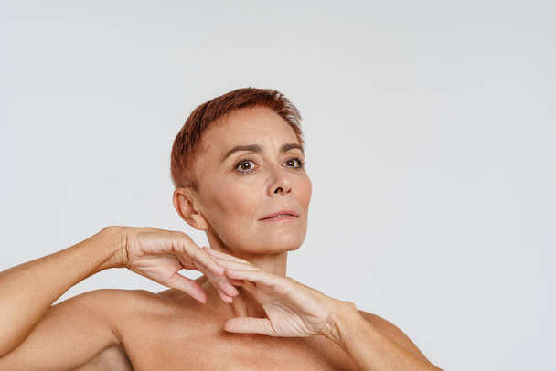 Senior shirtless woman with short hair gesturing and looking aside isolated over white background - Foto, afbeelding