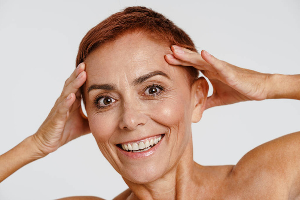 Senior shirtless woman with short hair smiling while holding her head isolated over white background - Foto, Bild