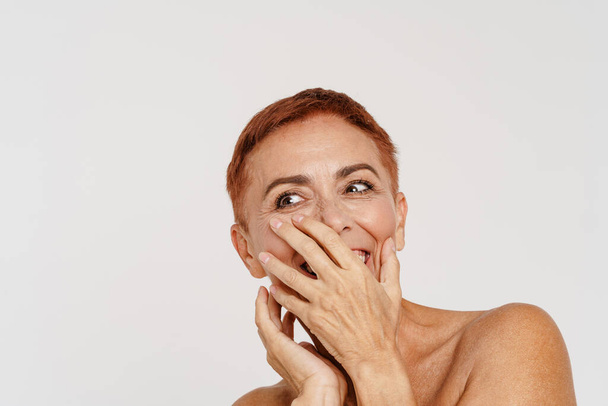 Senior shirtless woman with short hair laughing while covering her mouth isolated over white background - Fotó, kép