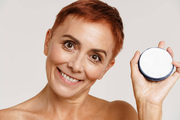 Senior shirtless woman with short hair showing face cream isolated over white background - Foto, immagini