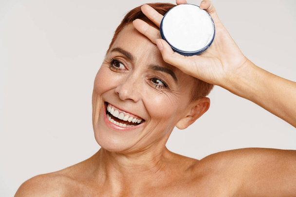 Senior shirtless woman with short hair showing face cream isolated over white background - Photo, image