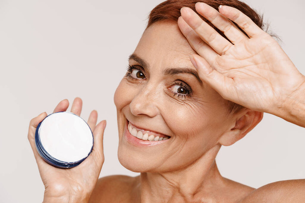 Senior shirtless woman with short hair showing face cream isolated over white background - Photo, Image