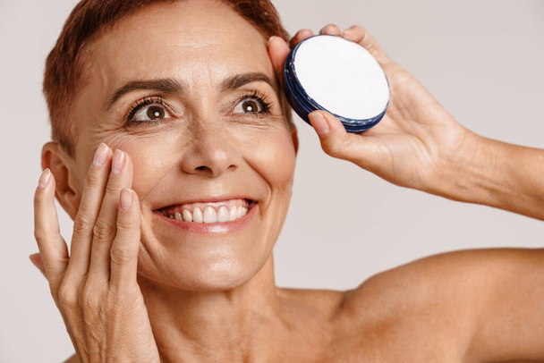 Senior shirtless woman with short hair showing face cream isolated over white background - Φωτογραφία, εικόνα