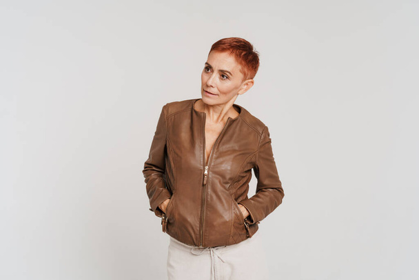 Ginger senior woman with short hair posing in leather jacket isolated over white background - Foto, Imagem