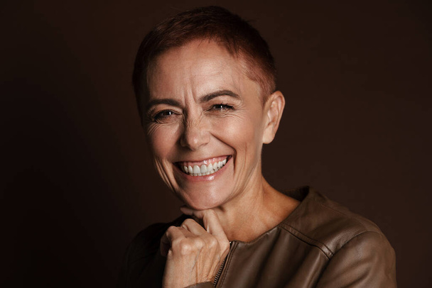 Senior ginger woman with short hair laughing and looking at camera isolated over brown wall - Foto, immagini