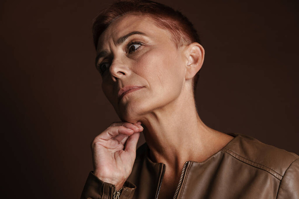 Senior ginger woman with short hair posing and looking aside isolated over brown wall - Φωτογραφία, εικόνα