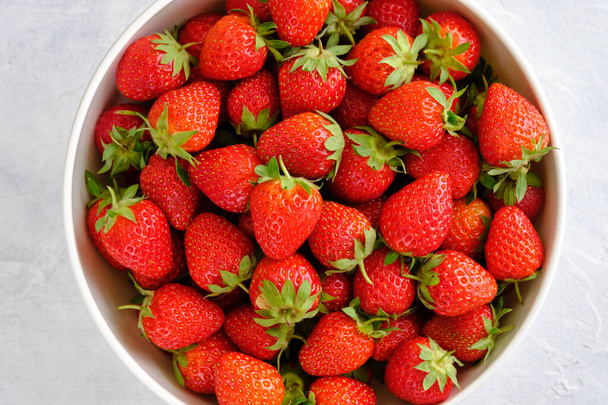 Sappige, heldere en zoete aardbeien in een kom op een witte betonnen tafel van dichtbij - Foto, afbeelding