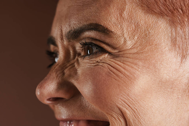 Senior mujer sin camisa sonriendo mientras posa en la cámara aislada sobre la pared marrón - Foto, Imagen