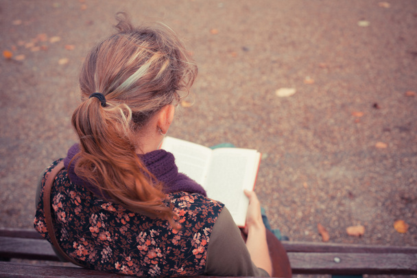 Young woman sitting on park bench with book - 写真・画像