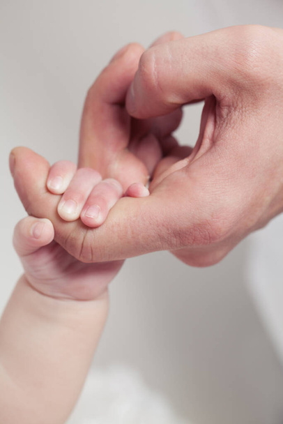 Adult hand holding her newborn baby's hand on white background. Childhood, family, birth concept - Foto, Imagem