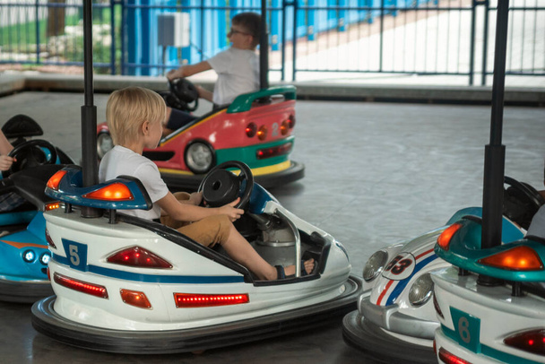 Jonge chauffeurs hebben plezier op de speelplaats voor kinderen op go kart race. Kinderen die botsauto rijden in het pretpark - Foto, afbeelding