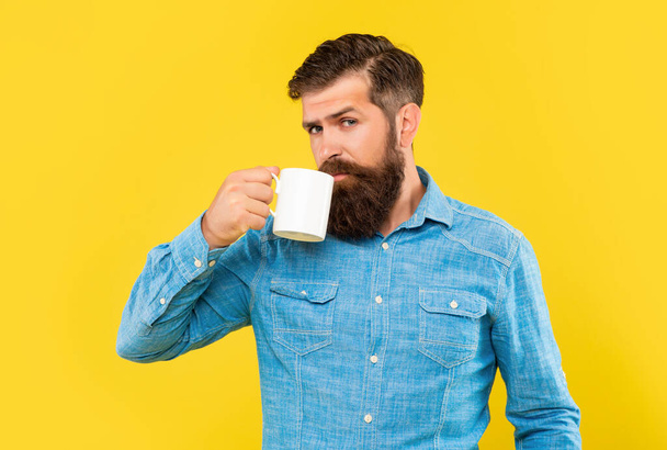 Serious caucasian guy drinking coffee from mug yellow background - Photo, image