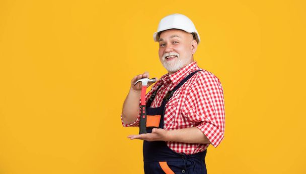 happy old aged man carpenter in helmet on yellow background - Fotó, kép