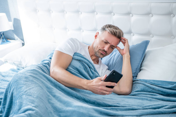 confused mature man in bed chatting on phone - Photo, Image