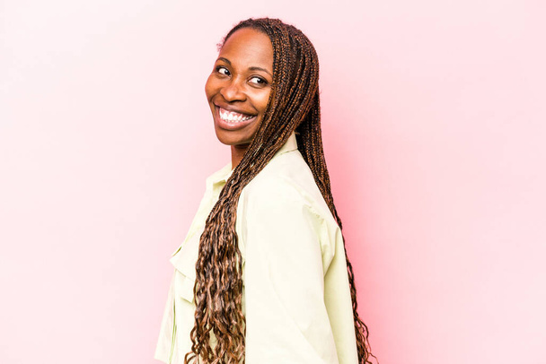 jonge afrikaanse amerikaanse vrouw geïsoleerd op roze achtergrond kijkt opzij glimlachend, vrolijk en aangenaam. - Foto, afbeelding