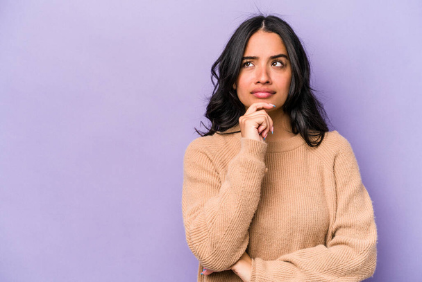 Young hispanic woman isolated on purple background looking sideways with doubtful and skeptical expression. - Photo, image