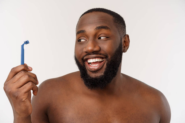 Primer plano de un hombre africano desnudo feliz afeitándose con navaja aislada sobre fondo gris
 - Foto, Imagen