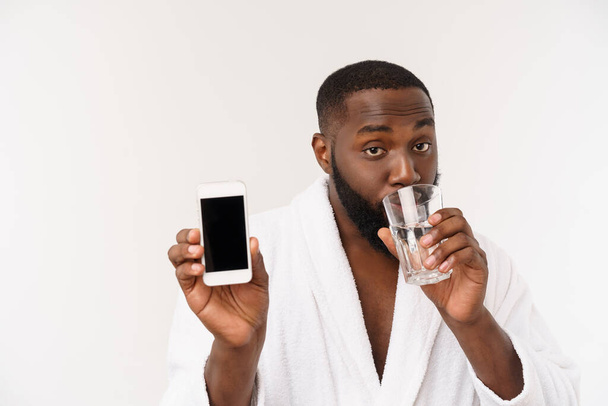 Hombre africano joven sediento sosteniendo agua potable de vidrio para la salud corporal aislado en el fondo blanco del estudio - Foto, imagen