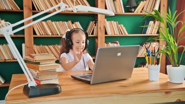Cute white preteen girl school kid child pupil wearing headphones raising hand distance learning online talking to camera at virtual lesson class by video conference call at home, webcam view. Sitting - Footage, Video