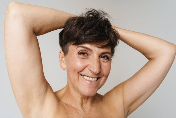Mature half-naked woman smiling while showing her armpits isolated over white background - Fotoğraf, Görsel