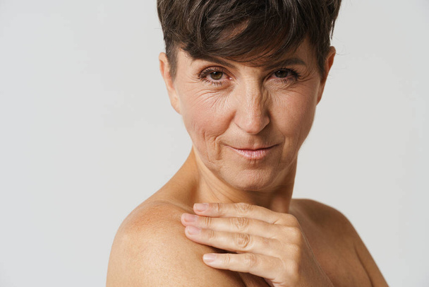 Mature half-naked woman smiling and touching her skin isolated over white background - Photo, image