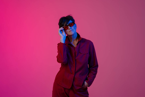 Mature european woman wearing sunglasses posing on camera isolated over pink background - Photo, Image