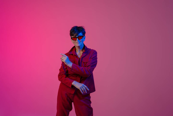 Mature european woman wearing sunglasses dancing on camera isolated over pink background - Foto, imagen