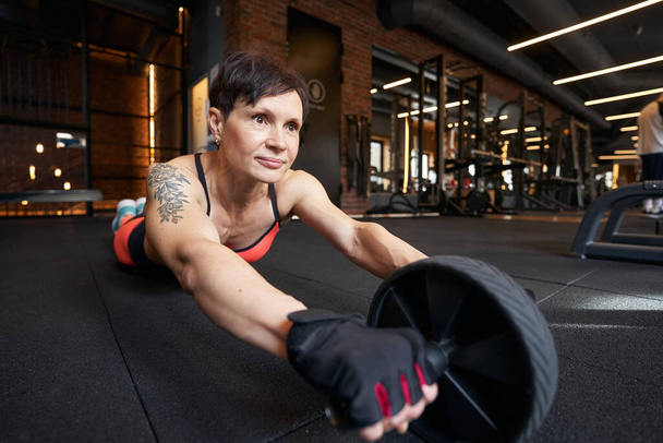 Sportswoman doing ab wheel rollout on gym floor - Valokuva, kuva