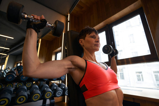Brawny woman working out with hand weights in fitness club - Fotografie, Obrázek