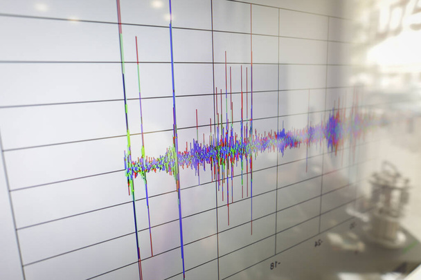 Shallow depth of field (selective focus) details with spikes on a seismogram on a digital display with the reflection of a device on the right. - Photo, Image