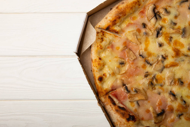 Smaczna włoska pizza z warzywami i kiełbaskami w pudełku na białym drewnianym tle. boczny widok. Miejsce do skopiowania. - Zdjęcie, obraz
