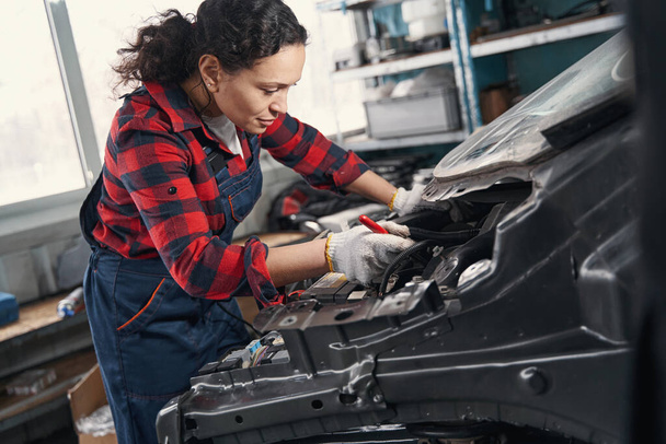 Young attentive female mechanic repairing car engine - Foto, afbeelding