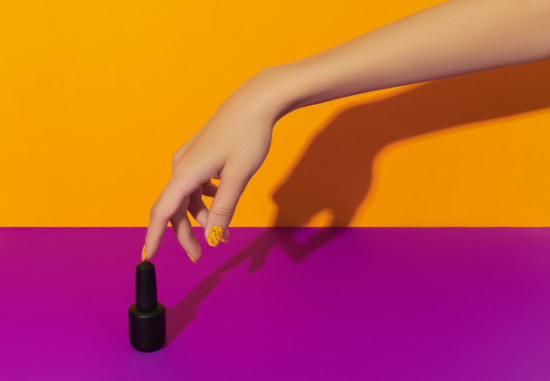Manicured womans hand with nail varnish bottle on purple table. Beauty salon template - Photo, Image