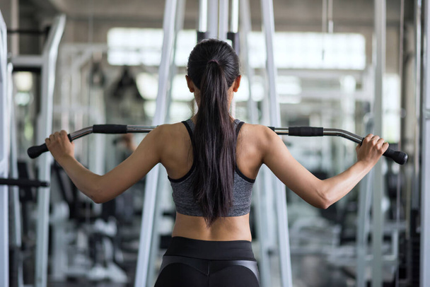 Hátul a fitt ázsiai fiatal nő gyakorolja szivattyúzás vissza fitnesz tornaterem. Testépítés és egészséges életmód középkorú nők számára. - Fotó, kép