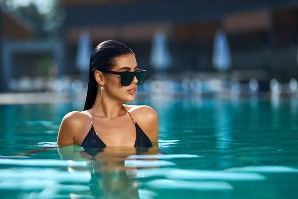 Fascinating female in sunglasses enjoying swimming in turquoise water of pool.  - Zdjęcie, obraz