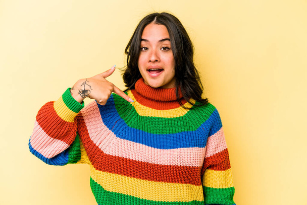 Молодая латиноамериканка, изолированная на желтом фоне, указывает рукой на пространство для копирования рубашки, гордая и уверенная в себе - Фото, изображение