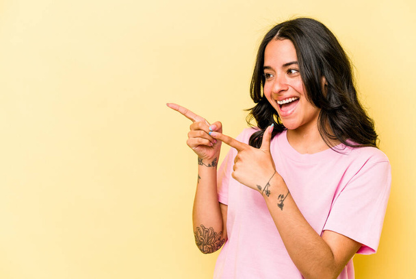 Young hispanic woman isolated on yellow background points with thumb finger away, laughing and carefree. - Photo, Image