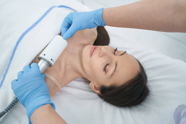 Esthéticienne fournissant des soins de la peau dans la zone du décolleté avec masseur endosphère pendant la thérapie cosmétique - Photo, image