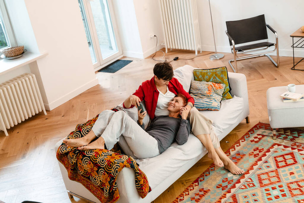 Mature lesbian couple using mobile phone while resting on sofa together at home - 写真・画像