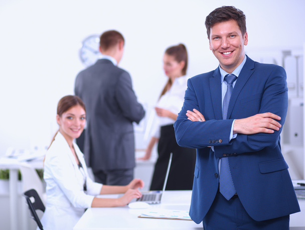 Menestyvä liikemies seisoo henkilöstönsä ollessa taustalla toimistossa
 - Valokuva, kuva