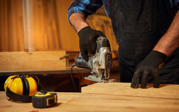 Close up of professional carpenter hands sawing wood with an electric jigsaw in the carpentry workshop - Zdjęcie, obraz