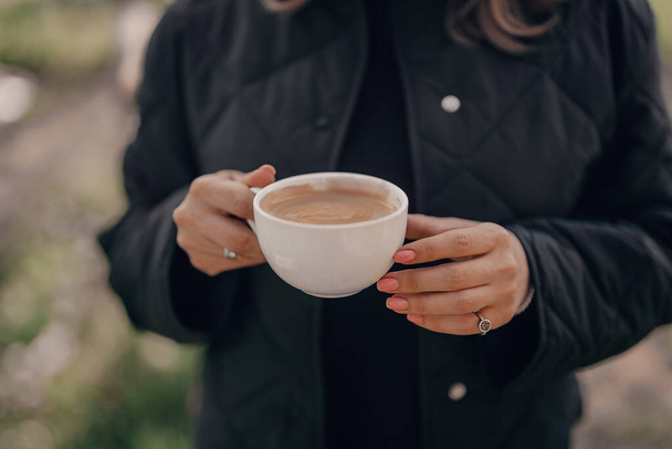 Female hands holding white porcelain cup of coffee. Fresh hot drink with foam from coffee-machine. Caffeine, energy, aroma concept - Photo, image