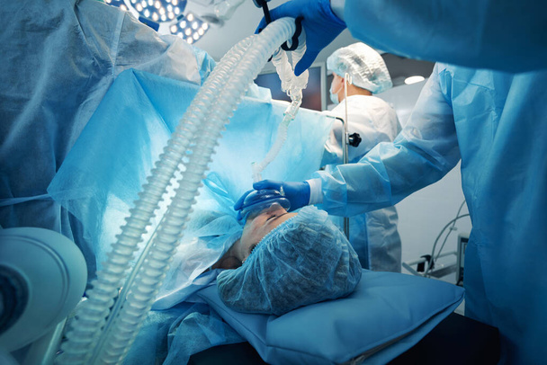 Χειρουργός πιέζοντας μάσκα της αναπνευστικής συσκευής οξυγόνου στο πρόσωπο του ασθενούς - Φωτογραφία, εικόνα